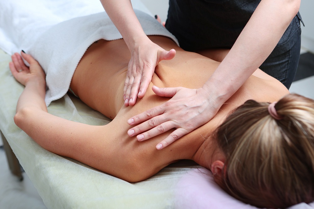 Masseur massages back and shoulder blades of young woman